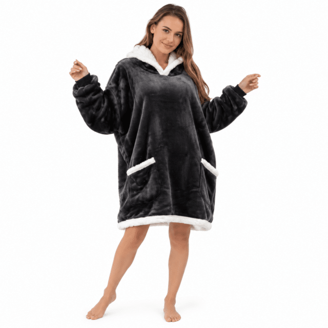 Vrouw spreidt haar armen in een zwarte oversized Snuggle hoodie deken met sherpa zakken